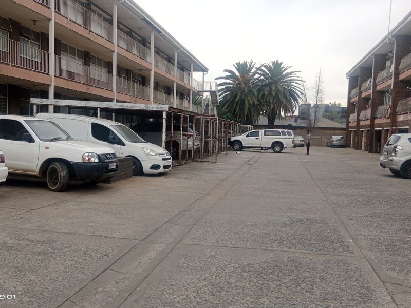 Exterior view of a multi-story residential flat complex featuring paved parking areas and covered parking bays.