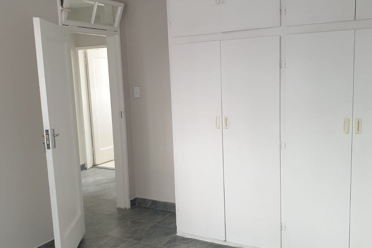 A vacant bedroom featuring built-in cupboards, grey tiled flooring, and a classic internal door with a transom window.