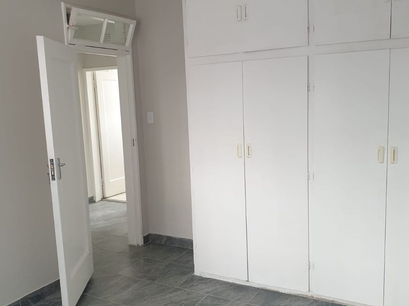 A vacant bedroom featuring built-in cupboards, grey tiled flooring, and a classic internal door with a transom window.