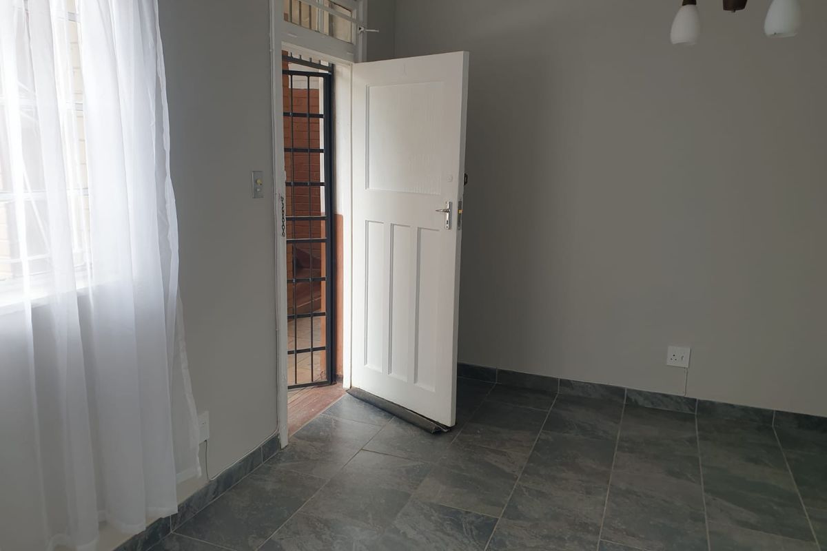 An empty living area featuring grey tiled flooring, neutral walls, and a secure entrance door with an integrated security gate.