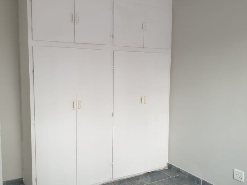 A clean, empty bedroom featuring built-in white cupboards and grey tiled flooring, providing a neutral canvas for personalization.