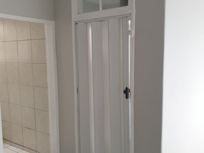 A clean, neutral-toned hallway featuring a folding door with a transom window and durable tiled flooring, providing access to adjacent tiled rooms.