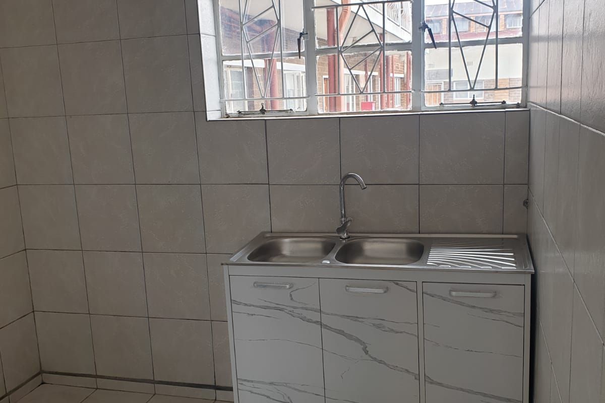 A functional kitchen area featuring tiled walls and flooring, equipped with a double bowl stainless steel sink and a window with security bars.