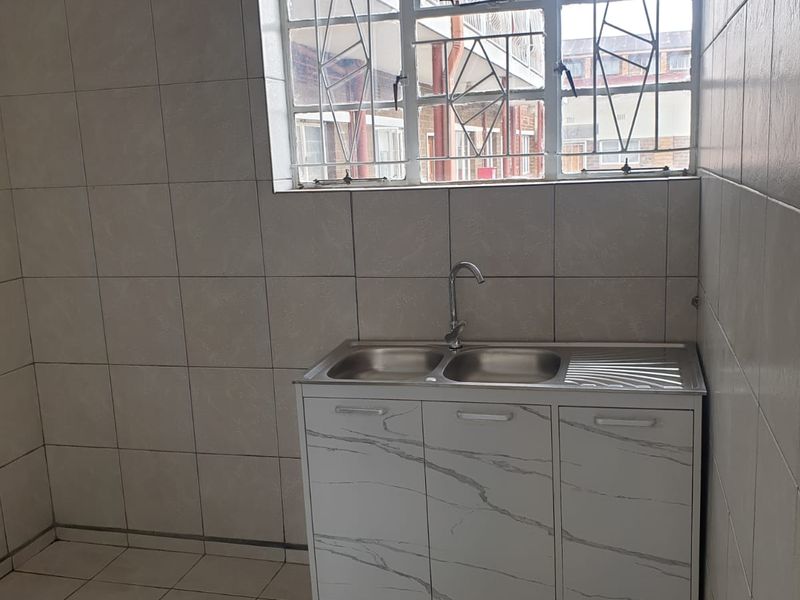 A functional kitchen area featuring tiled walls and flooring, equipped with a double bowl stainless steel sink and a window with security bars.