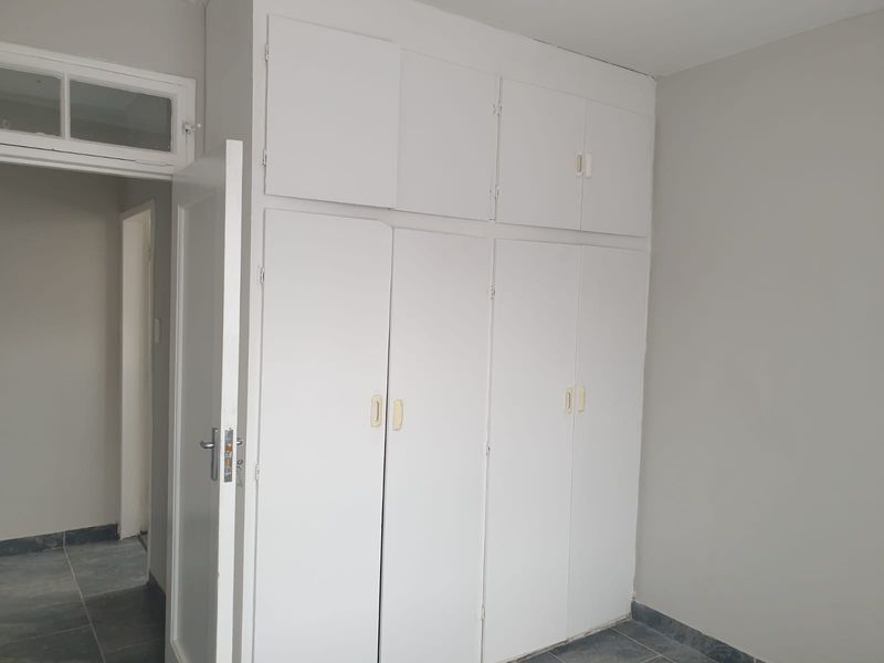 A bedroom featuring built-in floor-to-ceiling cupboards, tiled flooring, and a neutral color palette, offering a clean and functional space.