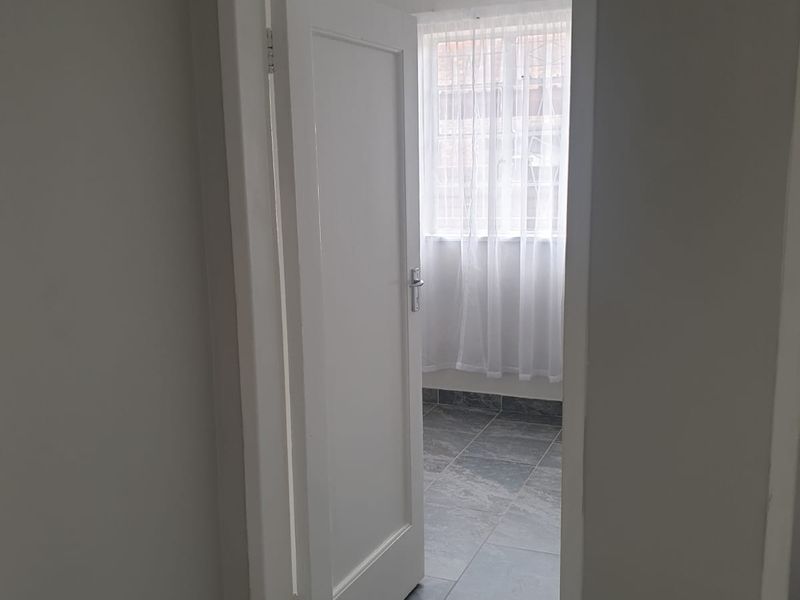 A clean, neutral hallway featuring grey tiled flooring and a classic internal door with a transom window above, leading into an adjacent room.