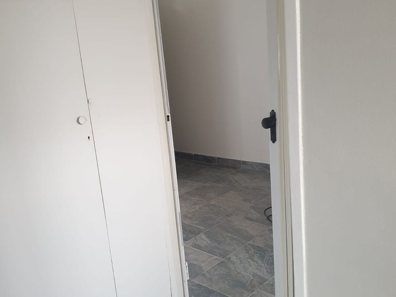 A view through a doorway into an empty room featuring grey tiled flooring and a built-in cupboard in the foreground.
