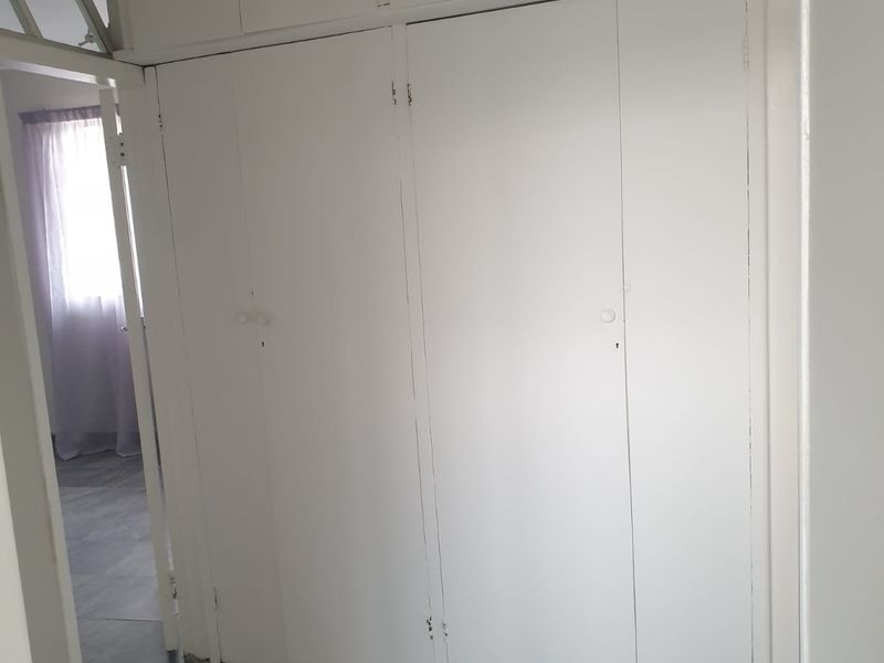 A hallway featuring built-in floor-to-ceiling storage cupboards with overhead cabinets and grey tiled flooring.
