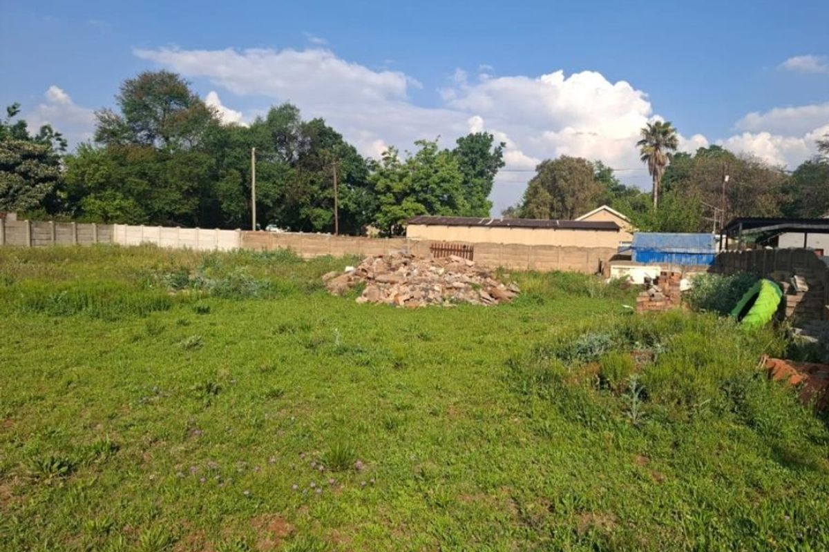 A vacant residential plot featuring a grassy area, perimeter boundary walling, and a pile of construction rubble requiring clearing.