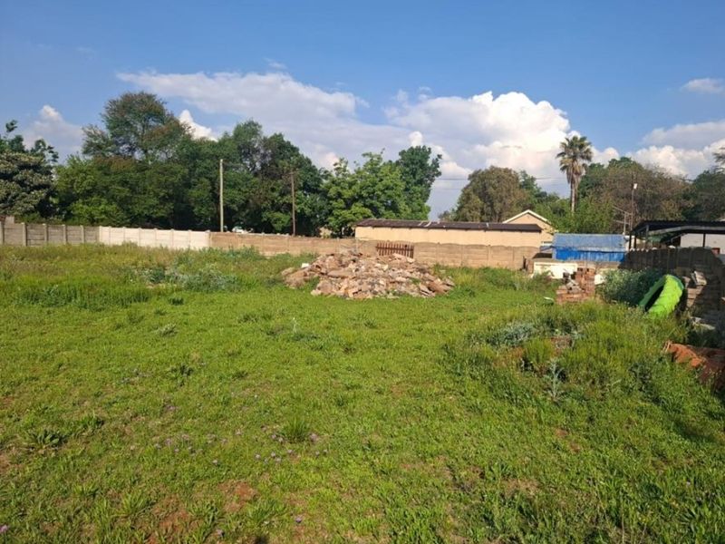 A vacant residential plot featuring a grassy area, perimeter boundary walling, and a pile of construction rubble requiring clearing.