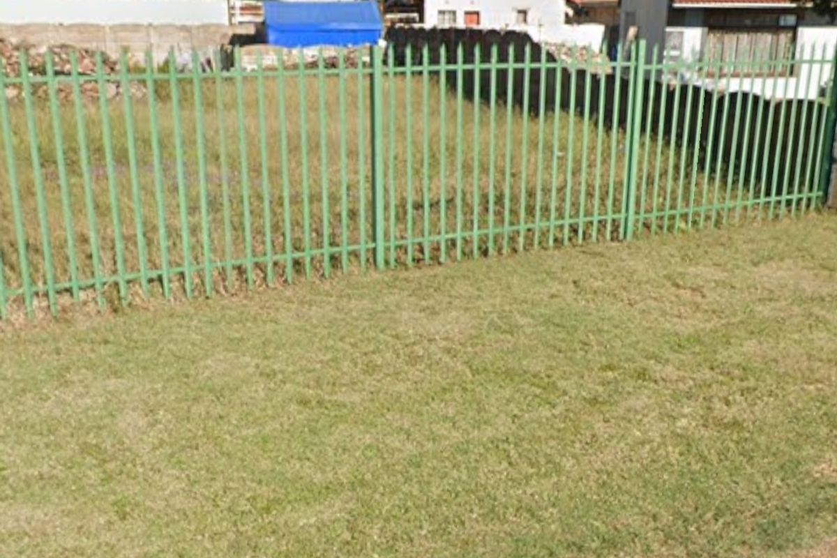 A view of the vacant residential land featuring green steel palisade fencing along the street boundary.