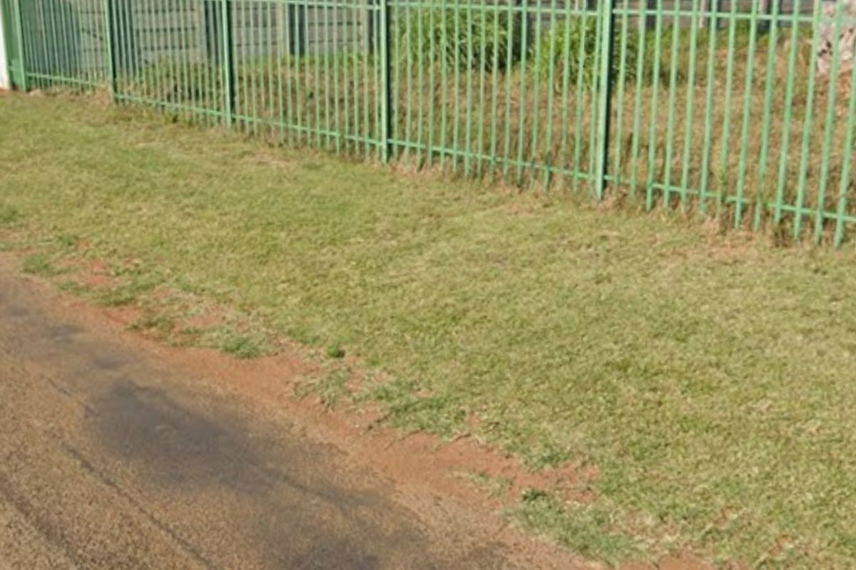 Street view of the property boundary featuring a metal palisade fence and adjacent paved road access.