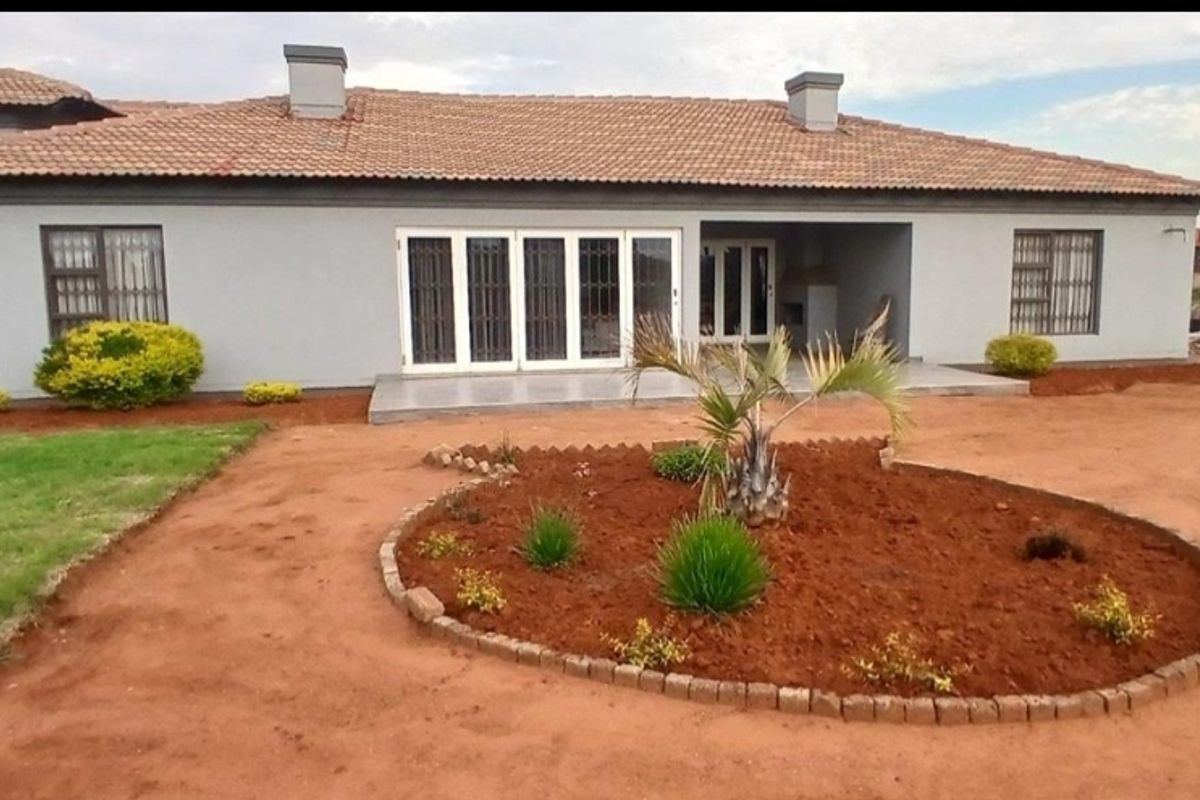 Rear view of a single-story house featuring a tiled roof, covered patio area, and a landscaped garden with a circular flower bed.