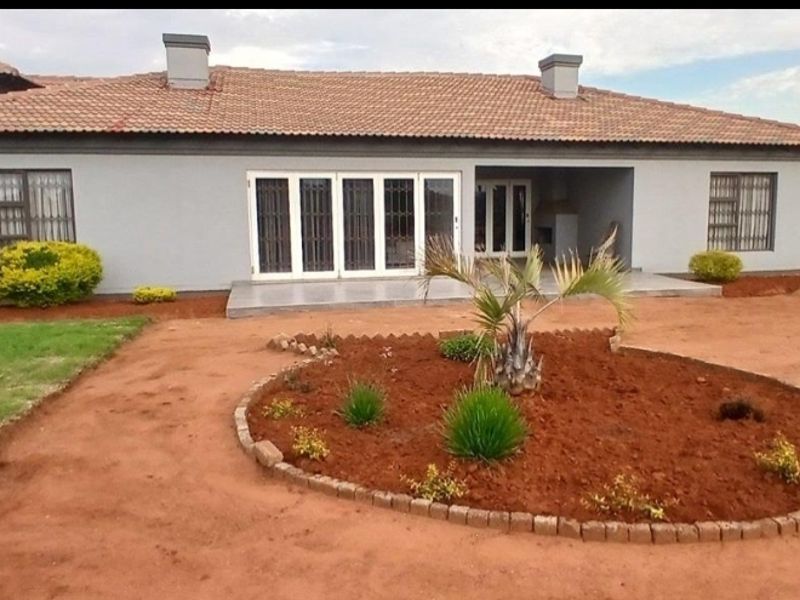 Rear view of a single-story house featuring a tiled roof, covered patio area, and a landscaped garden with a circular flower bed.