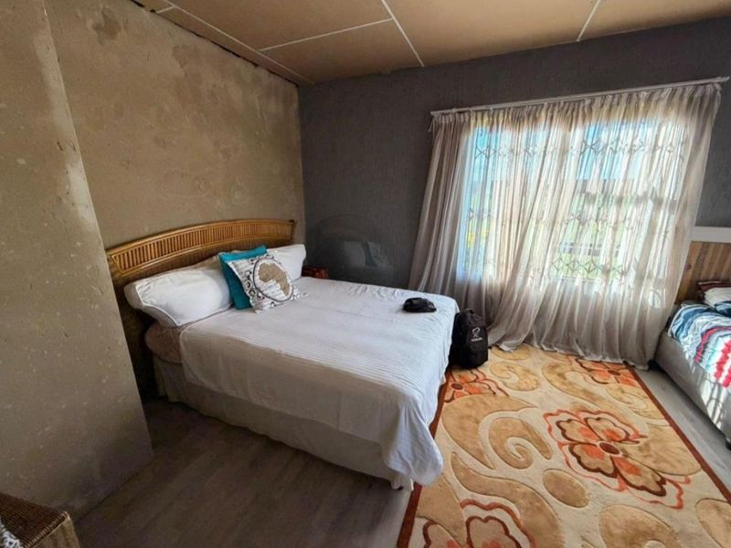 A bedroom featuring laminate flooring, security gate on the window, and textured wall finishes requiring cosmetic attention.
