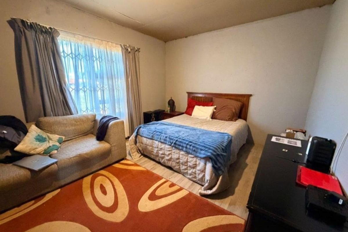 A bedroom featuring laminate flooring and a security gate on the window. The ceiling shows visible signs of staining and cracking.