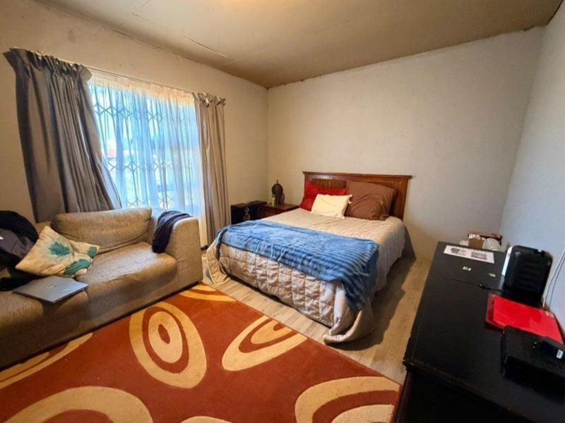 A bedroom featuring laminate flooring and a security gate on the window. The ceiling shows visible signs of staining and cracking.