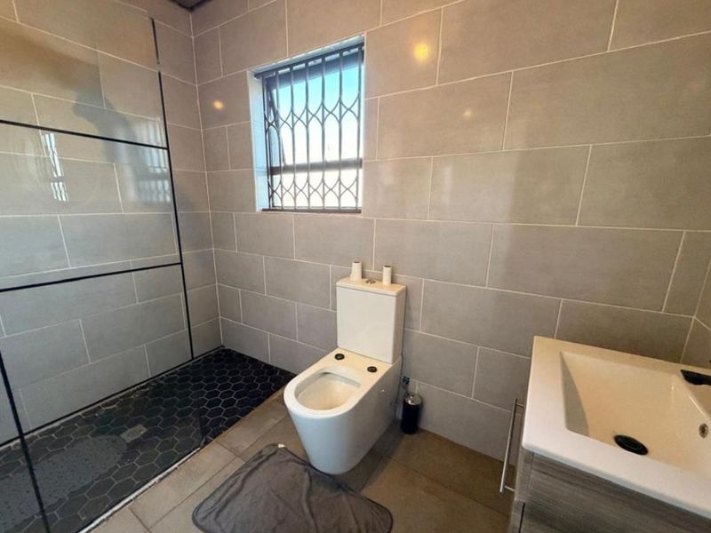 Modern bathroom featuring a walk-in shower with dark hexagonal floor tiles, a wall-mounted toilet, and a vanity basin with neutral wall tiling.