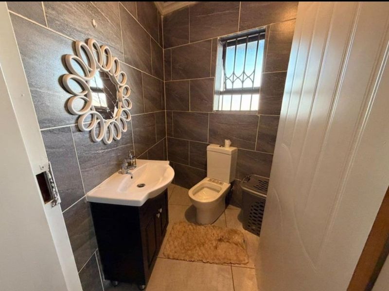A compact bathroom featuring modern dark grey wall tiles, a vanity cabinet with a basin, and a toilet with security bars on the window.
