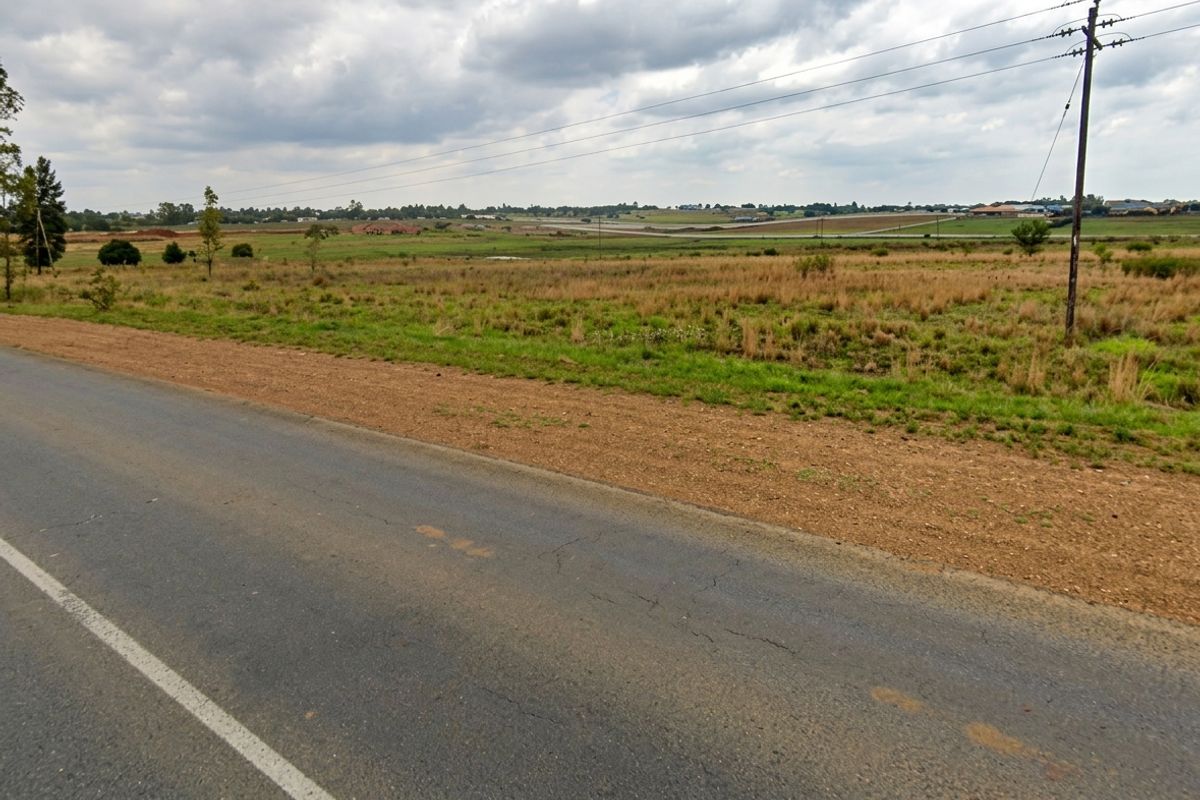 A view of the vacant residential land from the adjacent asphalt road, featuring overhead power lines and a utility pole.