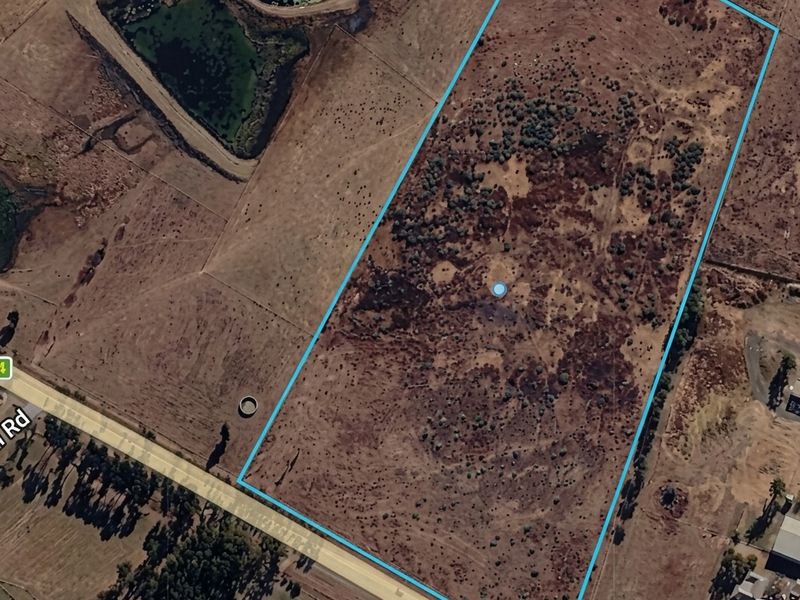 Aerial view of a large, vacant residential plot with natural vegetation and clear boundary lines, situated near a public road.