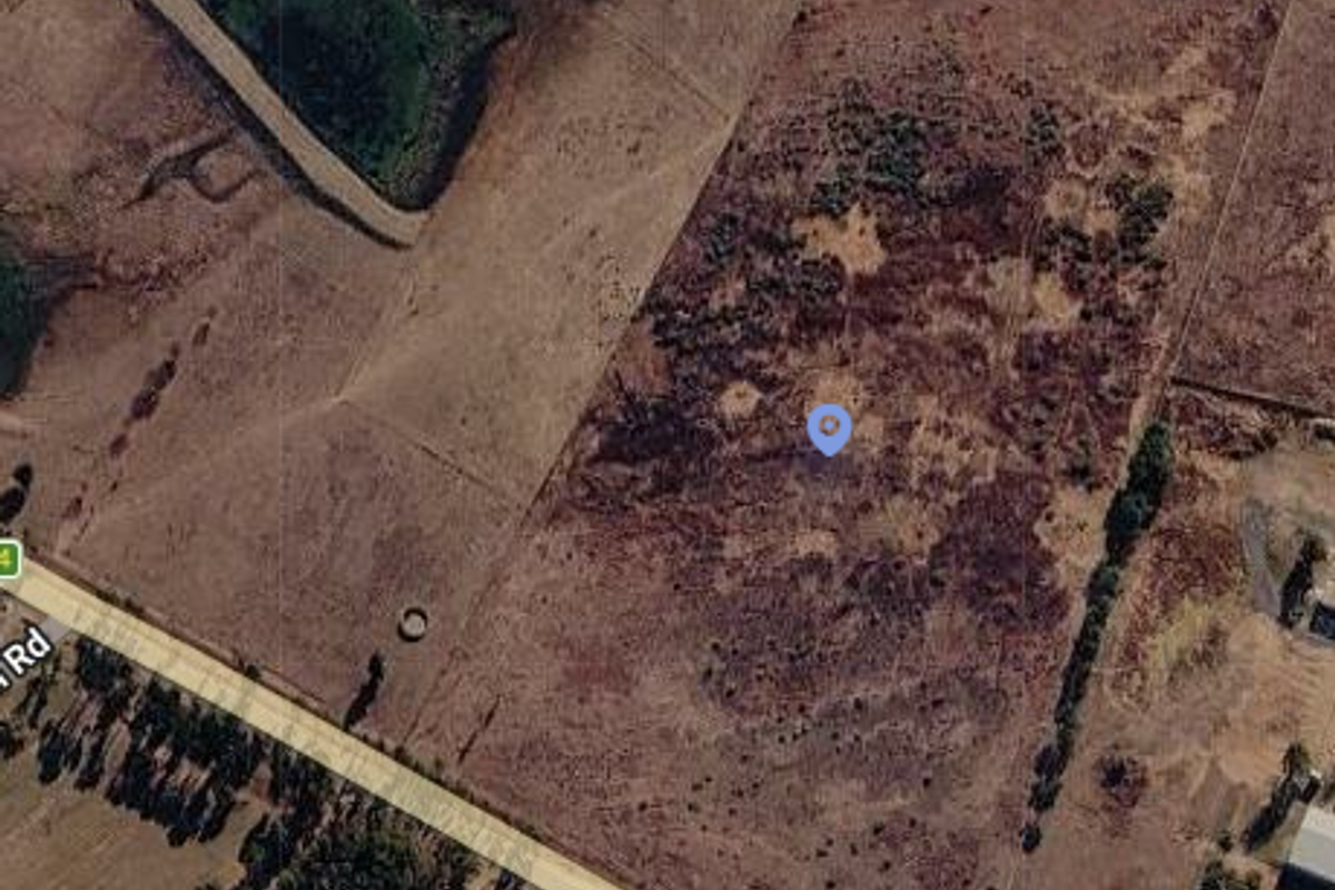 Aerial view of a large, undeveloped residential land parcel featuring natural vegetation and proximity to a main road.