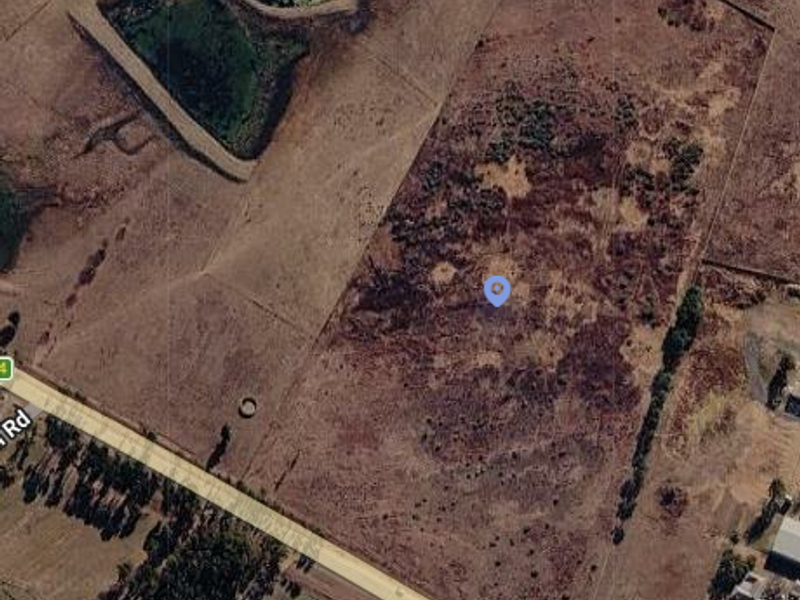 Aerial view of a large, undeveloped residential land parcel featuring natural vegetation and proximity to a main road.