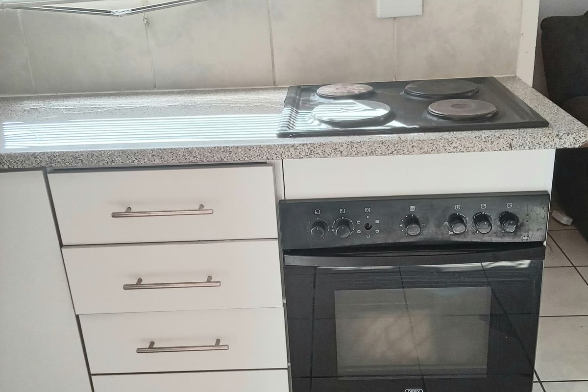 A compact kitchen area featuring a built-in oven, electric hob, granite countertops, and tiled backsplash with white cabinetry.