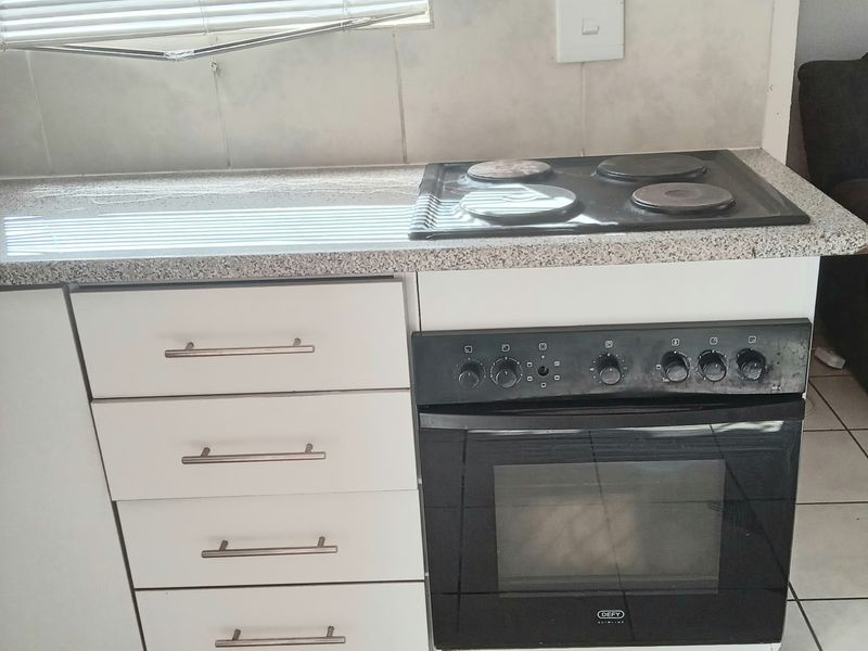 A compact kitchen area featuring a built-in oven, electric hob, granite countertops, and tiled backsplash with white cabinetry.