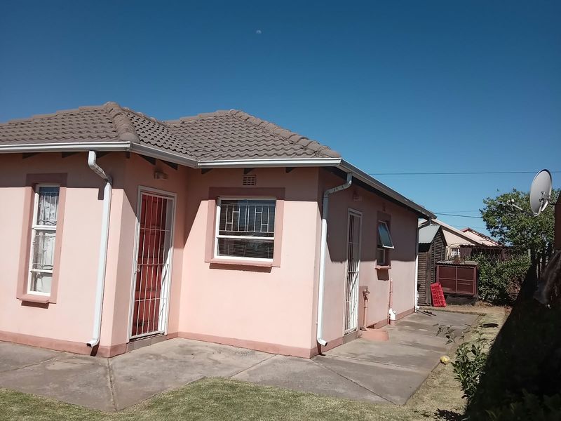 Rear view of a single-story house featuring a tiled roof, security gates, and concrete paved area.