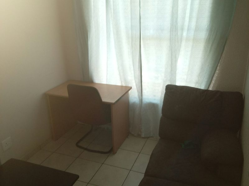 A small bedroom or study area featuring tiled flooring and a window with curtains.