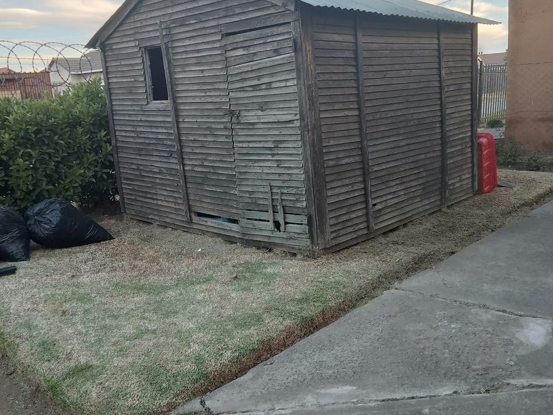 A weathered timber utility shed with a corrugated metal roof, situated on a concrete pathway in the backyard.