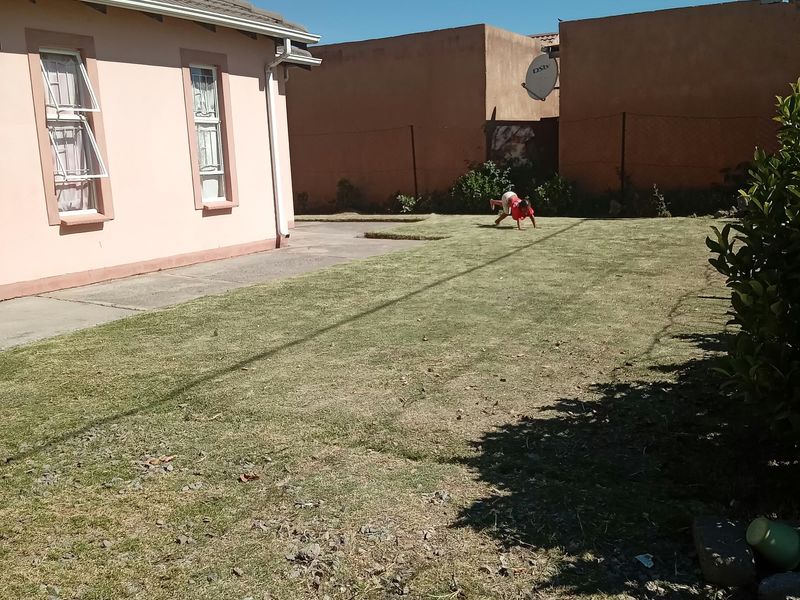 A rear exterior view of the property featuring a lawn area, concrete pathway, and perimeter walling.