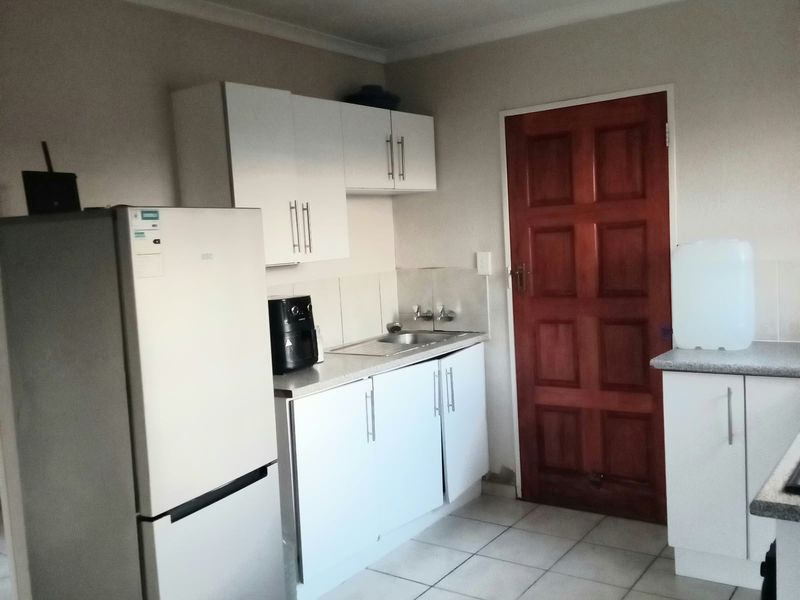 A functional kitchen featuring white cabinetry, a stainless steel sink, tiled backsplash, and tiled flooring, providing a practical workspace with direct access to an exterior door.
