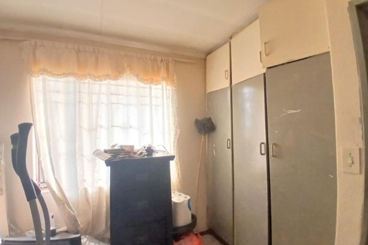A bedroom featuring built-in cupboards with overhead storage units, offering functional storage space in a dated interior setting.