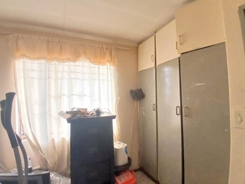 A bedroom featuring built-in cupboards with overhead storage units, offering functional storage space in a dated interior setting.