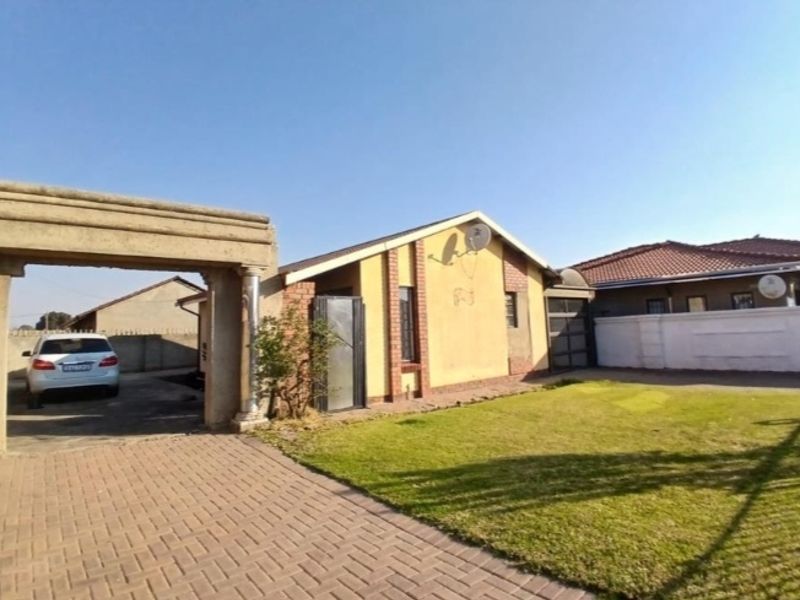 Front view of a residential property featuring a brick driveway, decorative stone entrance arch, and a lawn area.