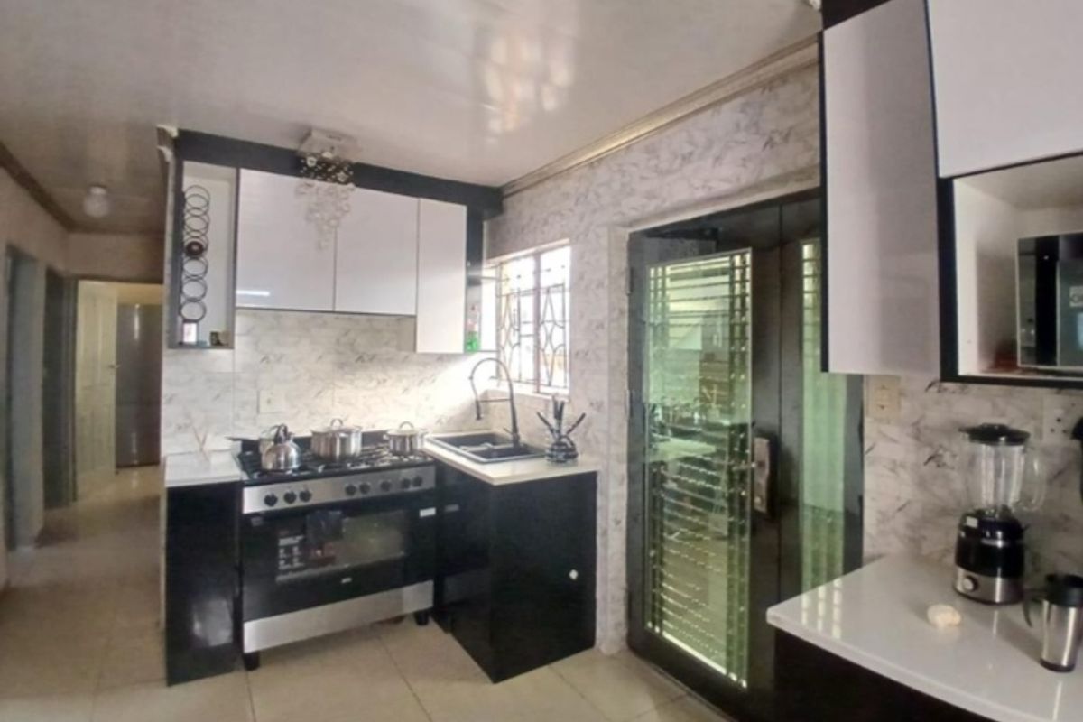 Modern kitchen featuring high-contrast black and white cabinetry, stone countertops, a gas stove with oven, and a secure glass-panelled door.