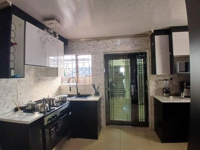 Modern kitchen featuring high-gloss cabinetry, a gas stove with extractor, tiled backsplash, and a secure glass-panelled exterior door.