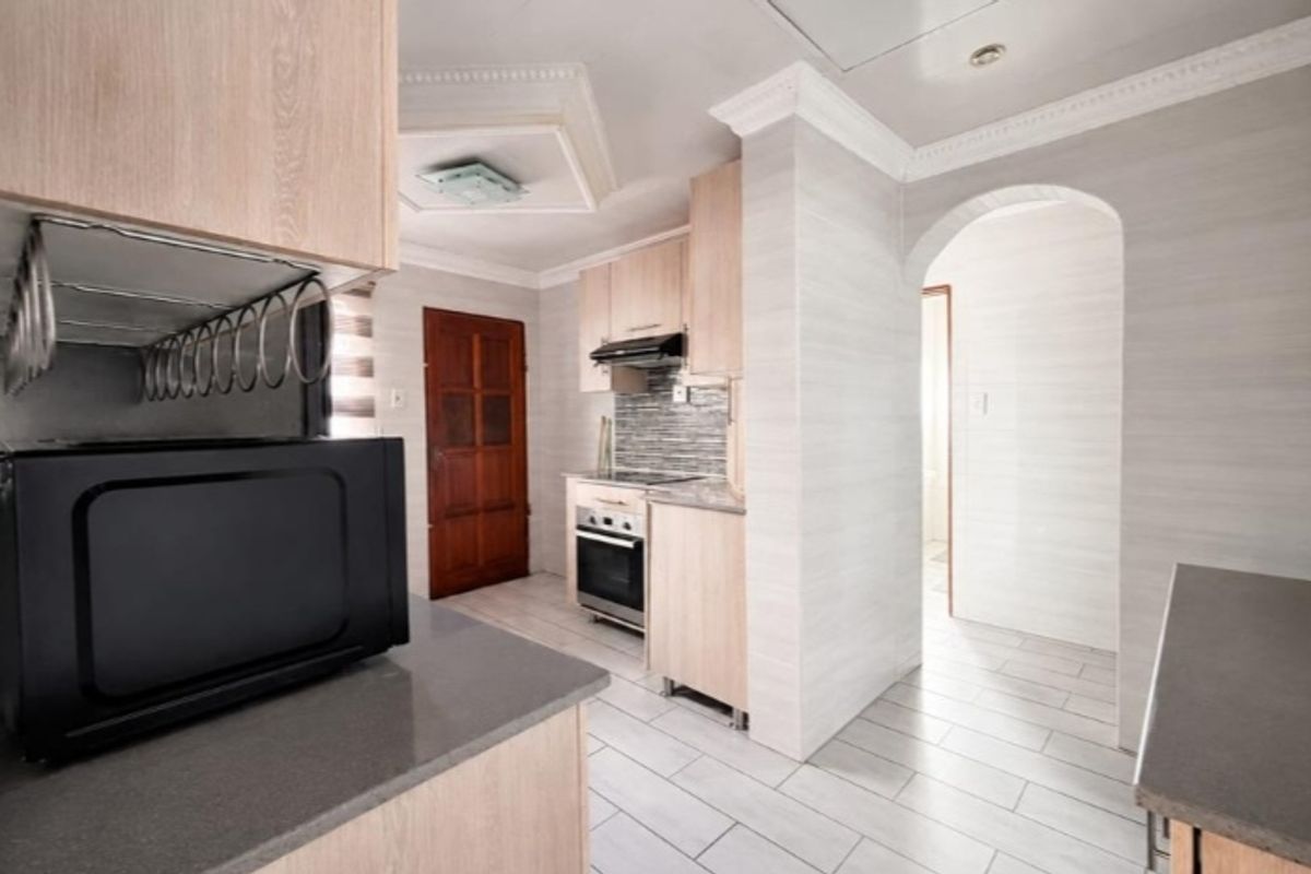 A functional kitchen featuring light wood cabinetry, modern tiled flooring, a built-in oven with extractor fan, and a classic arched entryway.