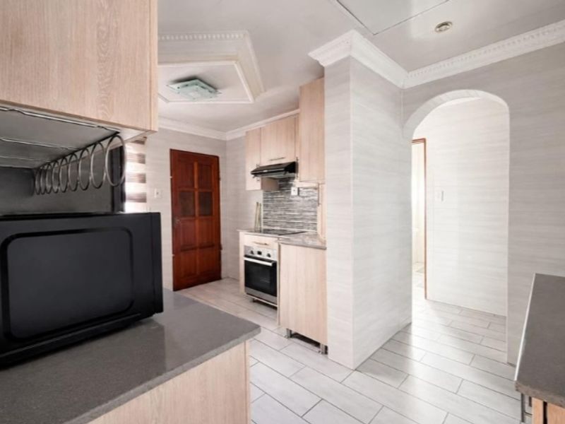 A functional kitchen featuring light wood cabinetry, modern tiled flooring, a built-in oven with extractor fan, and a classic arched entryway.