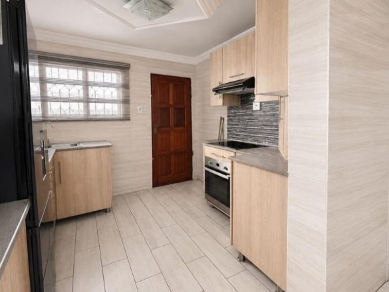 A functional kitchen featuring light wood cabinetry, a built-in oven and hob, tiled backsplash, and neutral floor tiles.