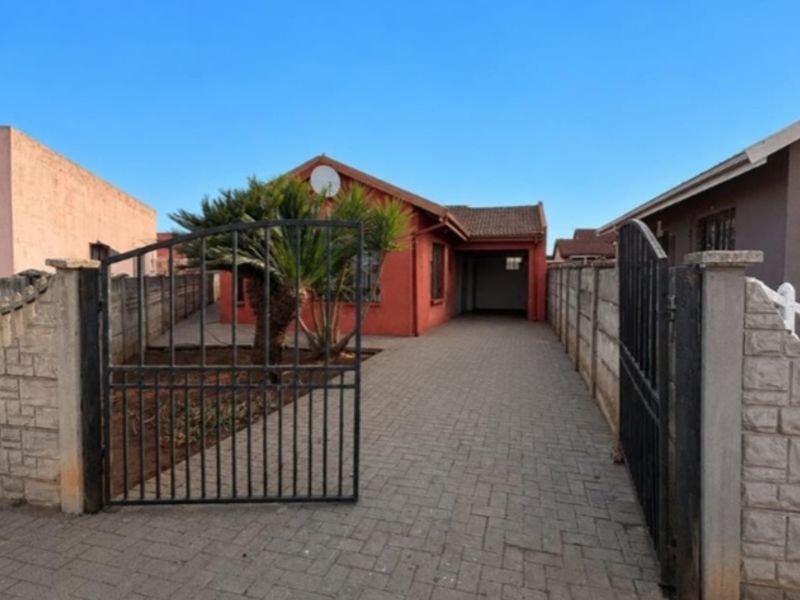 Front view of a residential property featuring a paved driveway, secure wrought iron gate, and precast concrete boundary walls.