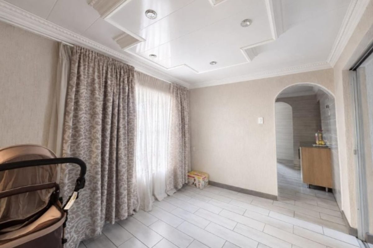 A bright living area featuring tiled flooring, a decorative recessed ceiling with downlights, and an arched entryway leading to an adjacent space.