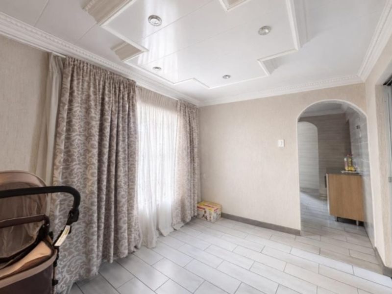 A bright living area featuring tiled flooring, a decorative recessed ceiling with downlights, and an arched entryway leading to an adjacent space.
