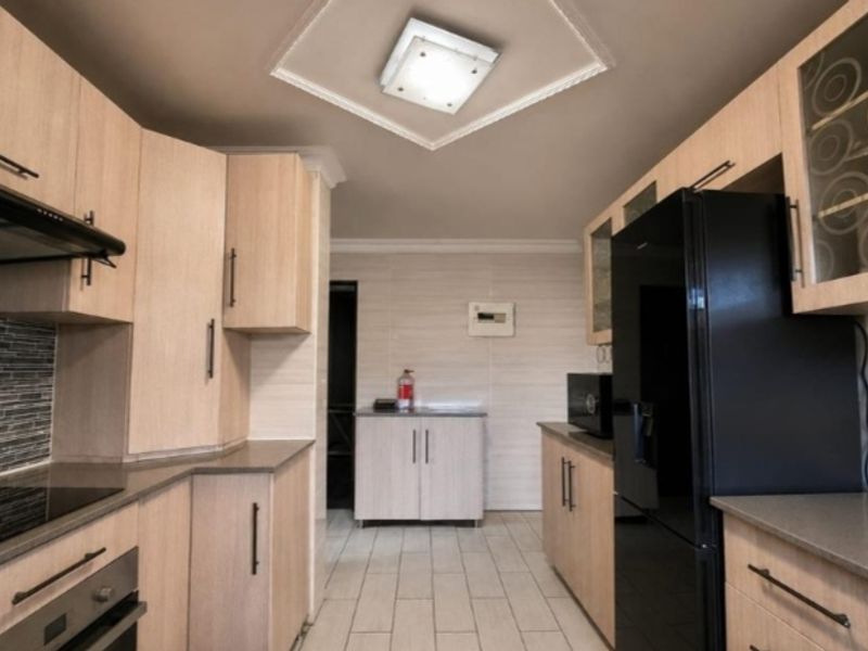 A well-maintained kitchen featuring light wood cabinetry, stone countertops, a tiled backsplash, and integrated appliances with a modern ceiling design.