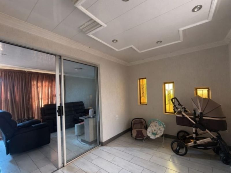 A bright living area featuring tiled flooring, decorative ceiling molding with recessed lighting, and sliding glass doors leading to an adjacent room.