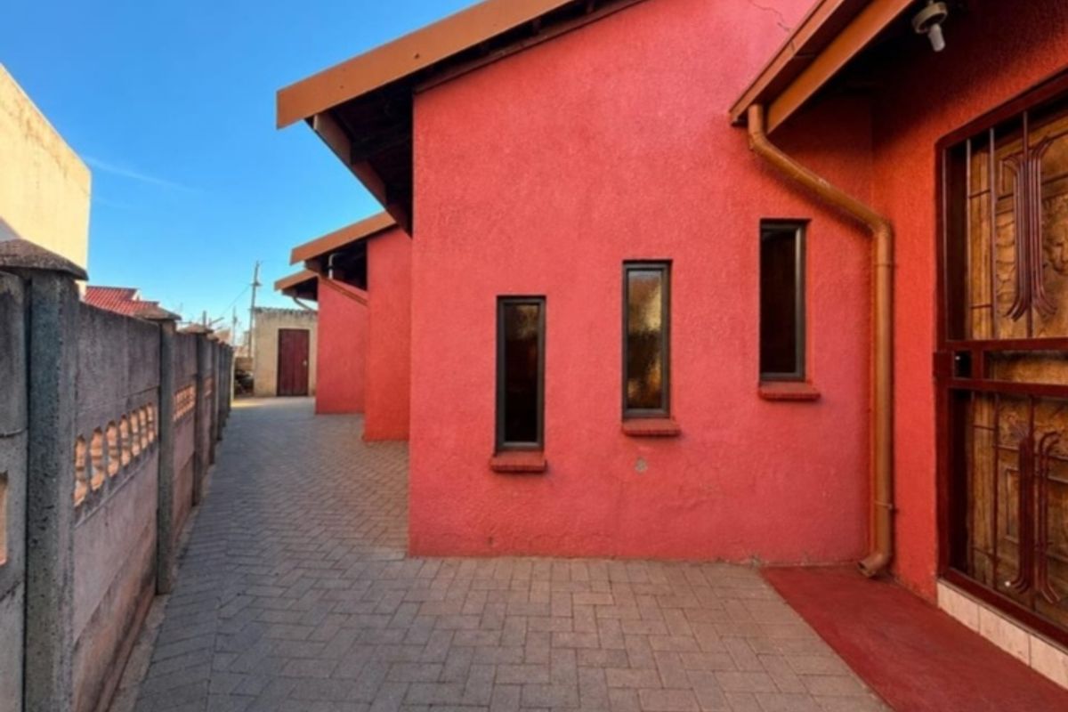 A side view of the property featuring a paved walkway, textured red exterior walls, and a secure boundary wall.
