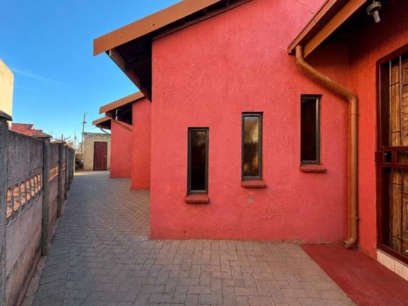 A side view of the property featuring a paved walkway, textured red exterior walls, and a secure boundary wall.