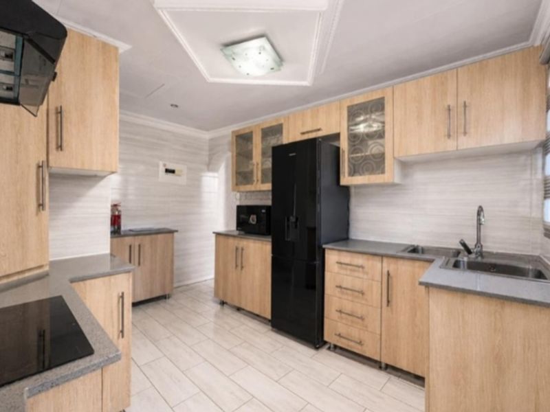 A well-maintained kitchen featuring light wood cabinetry, grey stone countertops, integrated hob, extractor fan, and tiled flooring with modern finishes.